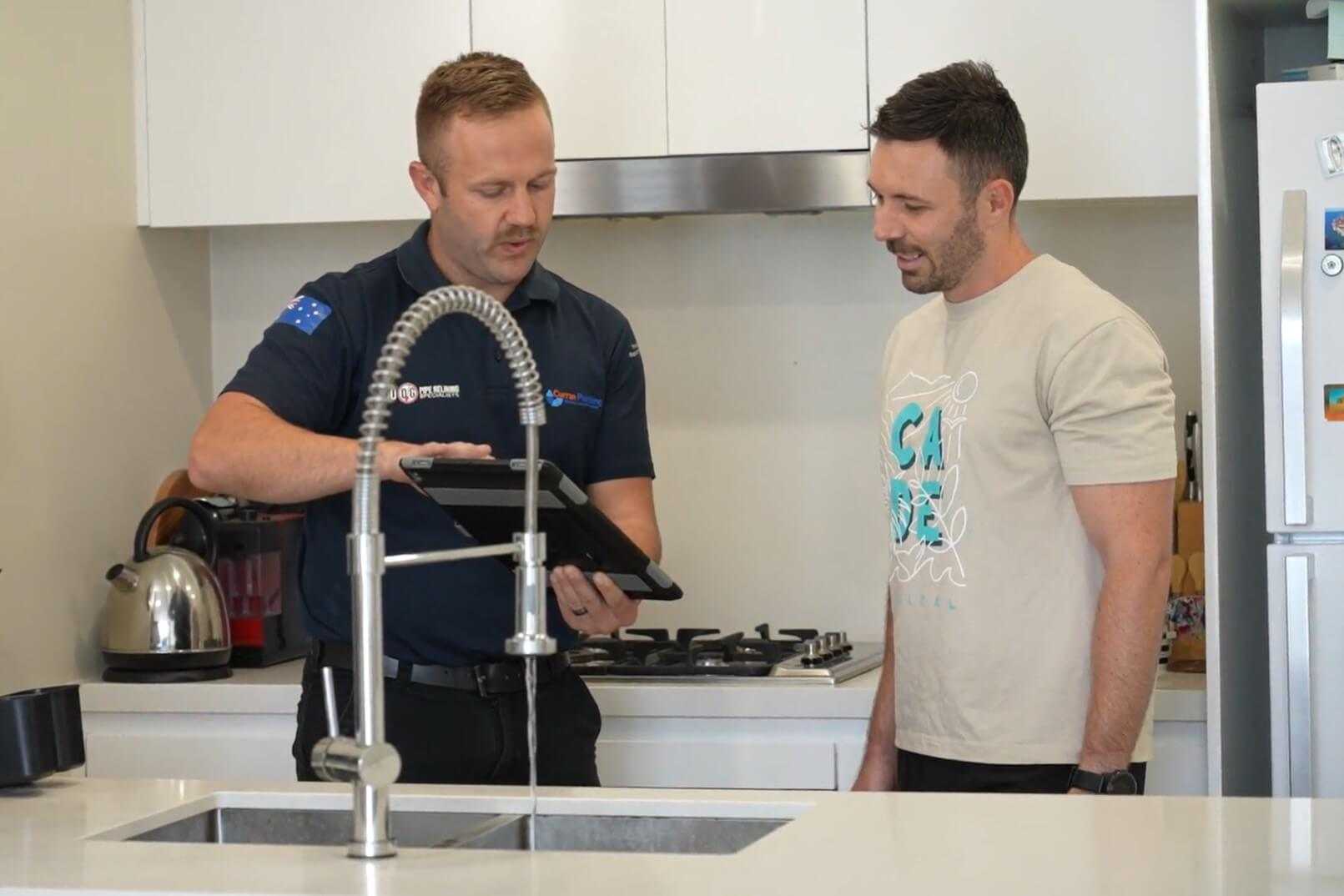 Plumber showing tablet to client in front of kitchen sink