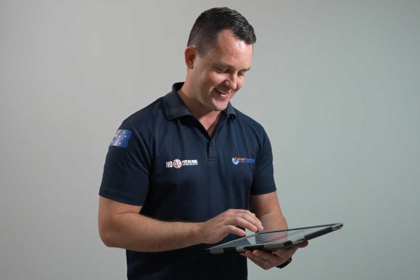Plumber wearing navy top looking at FlatRateNOW on a tablet